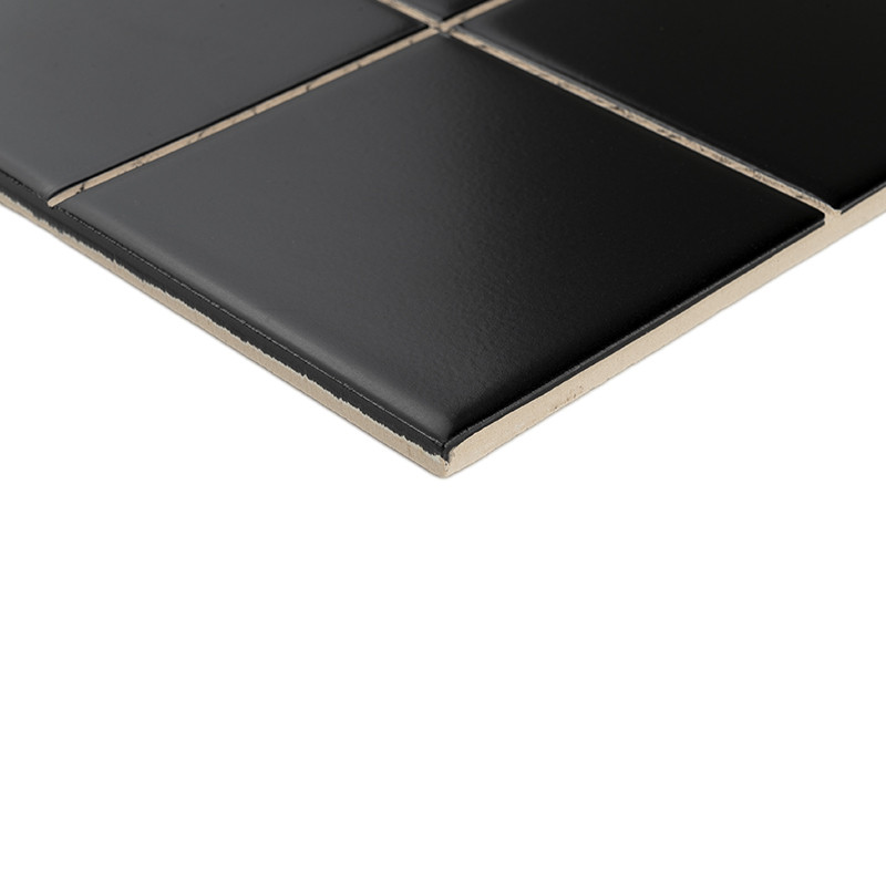 Black glazed tile, slightly glossy surface and beveled edge; light grout joints forming a cross, arranged in a corner on a white background, showing thickness and profile.