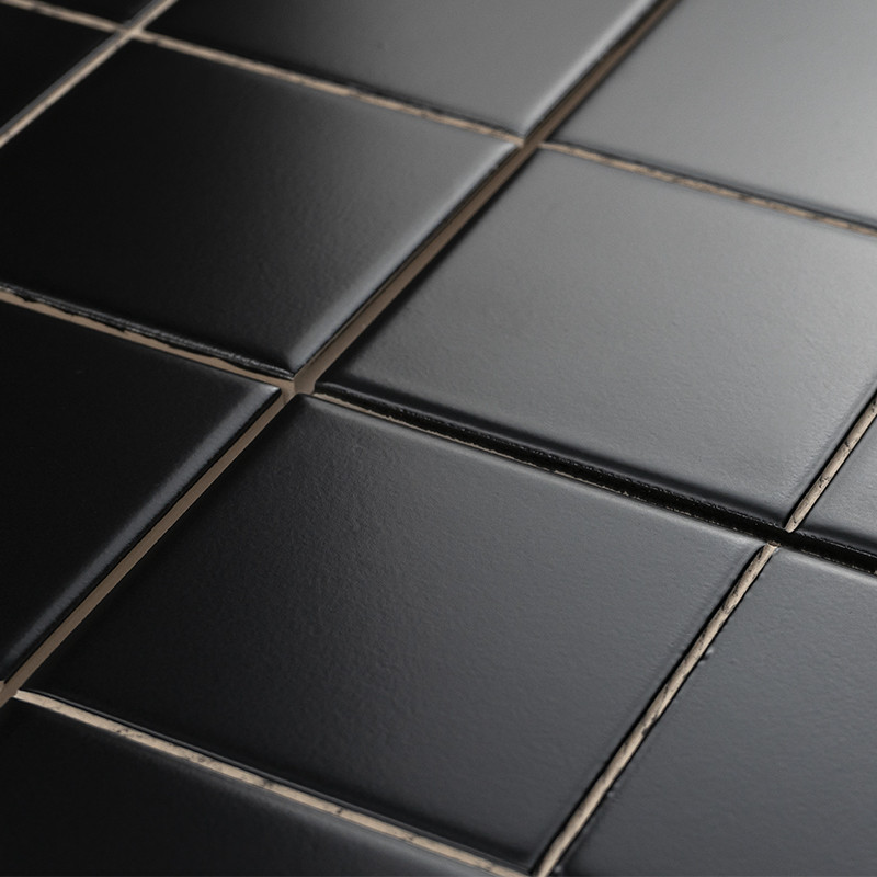 Azulejos negros cuadrados con acabado semibrillante, separados por juntas claras y finas; primer plano en perspectiva que resalta textura lisa y reflejos suaves.