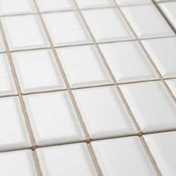 White ceramic tiles are neatly arranged in a grid pattern, slightly elevated at their centers, creating a textured, geometric su