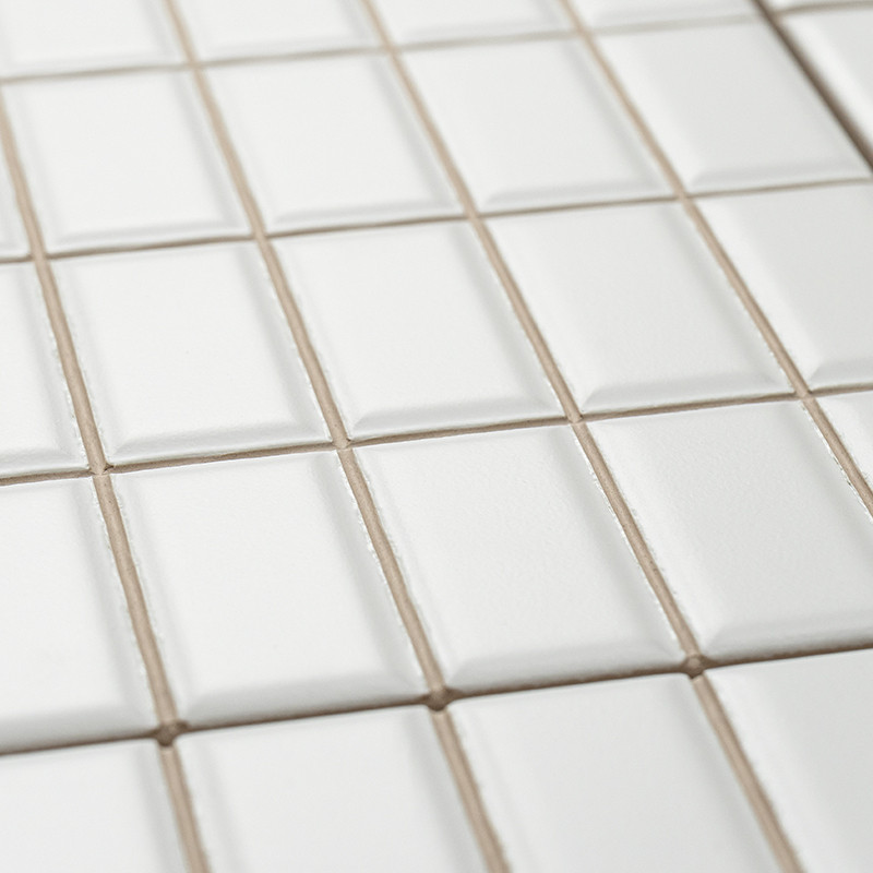 Les carreaux de céramique blanche sont soigneusement disposés selon un motif en grille, légèrement surélevés en leur centre, cré