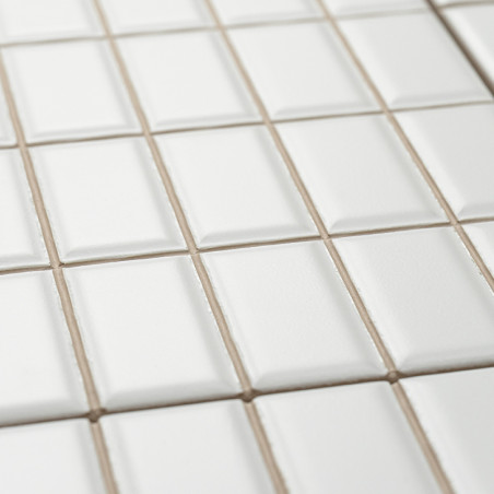 White ceramic tiles are neatly arranged in a grid pattern, slightly elevated at their centers, creating a textured, geometric su