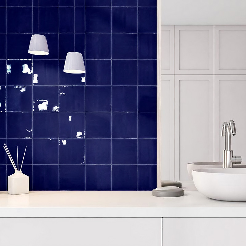 Blaue quadratische Fliesen schmücken eine Wand und reflektieren das Licht subtil. In der Nähe befindet sich unter zwei Pendelleu