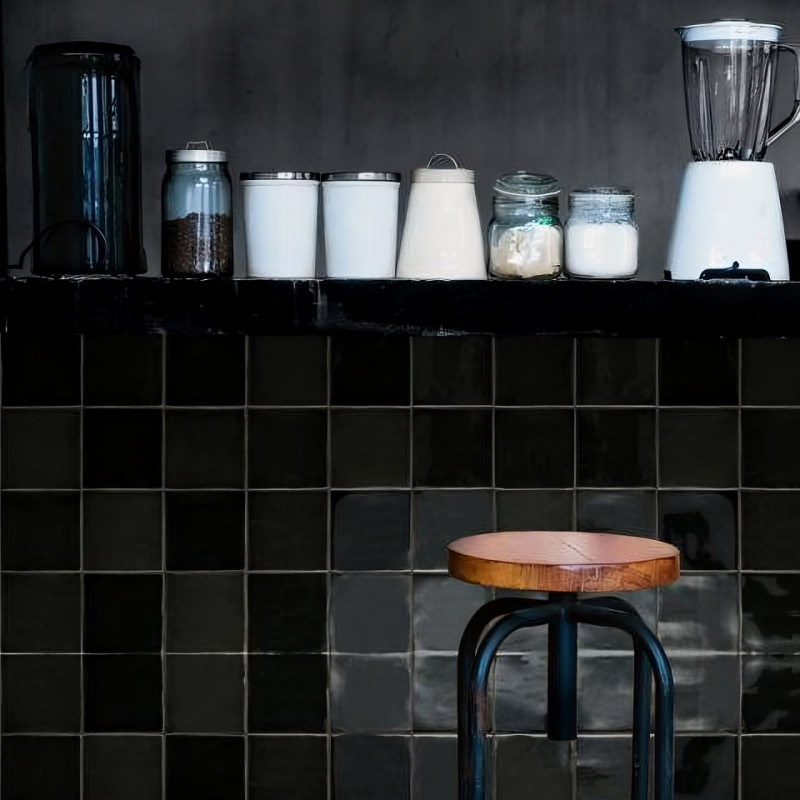 En la encimera de la cocina hay una licuadora, frascos y un recipiente. Debajo, un taburete de madera se alza contra las paredes