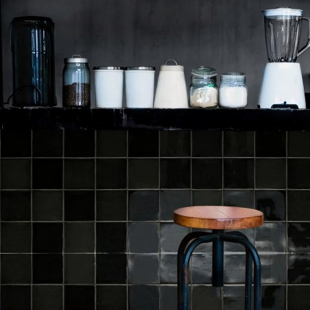 Op een aanrecht staan een blender, potten en een jerrycan. Beneden staat een houten kruk tegen donker betegelde muren. Op een aanrecht staan een blender, potten en een jerrycan. Beneden staat een houten kruk tegen donker betegelde muren.