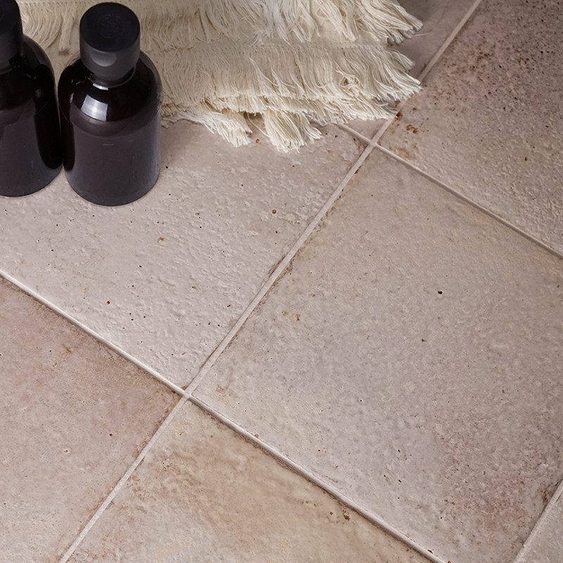 Dos botellas oscuras con tapa se encuentran sobre azulejos beige con superficies texturizadas. Cerca hay una tela blanquecina co