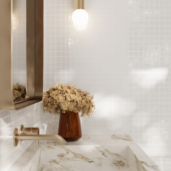A brown vase holds dried flowers, standing on a marble sink. Above, a glowing bulb casts light in a tiled bathroom.