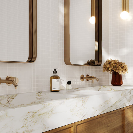 Brown wall-mounted faucets extend over a white marble sink with gold veining. Two mirrors are above, flanked by modern pendant l