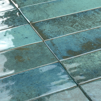 Des carreaux rectangulaires brillants dans des tons de bleu et de vert se côtoient, réfléchissant la lumière dans une surface te