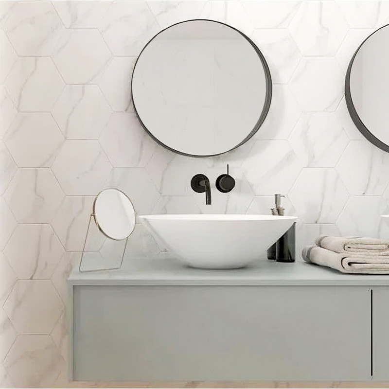 A round mirror hangs on a bathroom wall, above a modern white sink. The setting includes minimalistic decor and hexagonal wall t