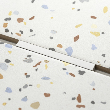 Speckled terrazzo tile, displaying scattered colorful flecks, lies adjacent to another tile with a visible straight grout line, 