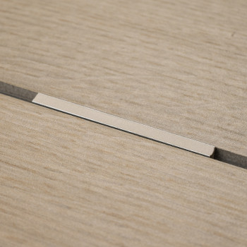 Un carreau beige à texture de bois repose à plat avec une étroite bande métallique encastrée dans une rainure centrale, contre u