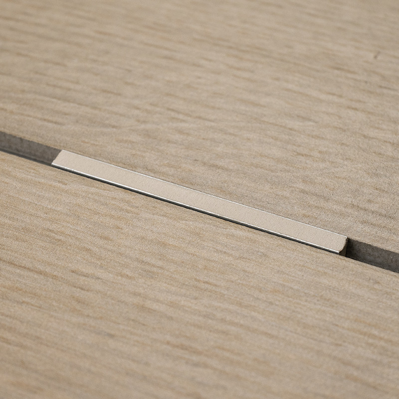 Un azulejo con textura de madera de color beige queda plano con una estrecha tira metálica incrustada en una ranura central, col