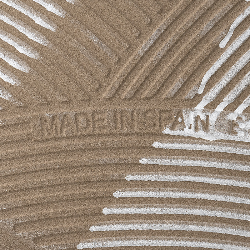 The tile, with a textured surface, displays the text `MADE IN SPAIN` against a background of swirling, raised lines.