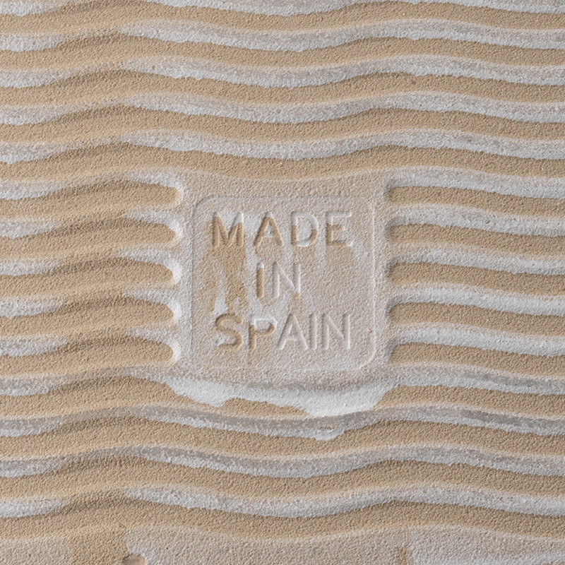 Azulejo textura arena con grabado `MADE IN SPAIN`. Los patrones ondulados crean un efecto ondulado, sugiriendo un ambiente parec