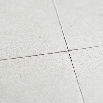 Quatro ladrilhos cerâmicos cinza claro se cruzam nos cantos, formando um padrão cruzado. A superfície tem um acabamento sutil e 