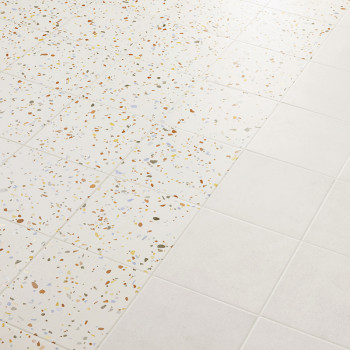 Tiles transition from terrazzo, speckled with multicolored chips, to plain white, creating a pattern on the smooth floor surface