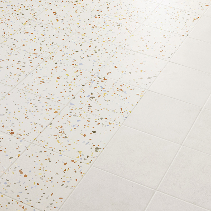 De tegels gaan over van terrazzo, gespikkeld met veelkleurige chips, naar effen wit, waardoor een patroon op het gladde vloeropp