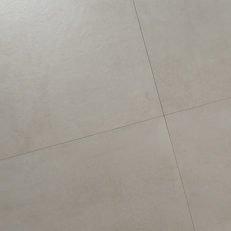 Carrelage clair à grands carreaux carrés, joints fins formant une croix, surface lisse légèrement texturée, tons beige-gris neutres, plan oblique montrant angle de quatre carreaux.