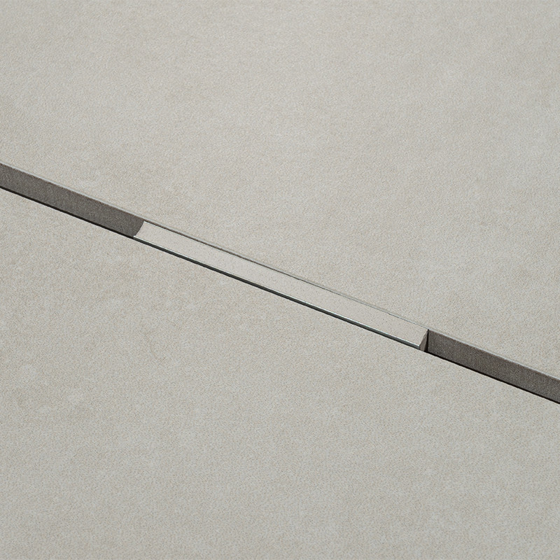 Carrelage clair mat présentant une rainure diagonale : encoche rectangulaire sombre de chaque côté et bande brillante centrale, vue en gros plan.