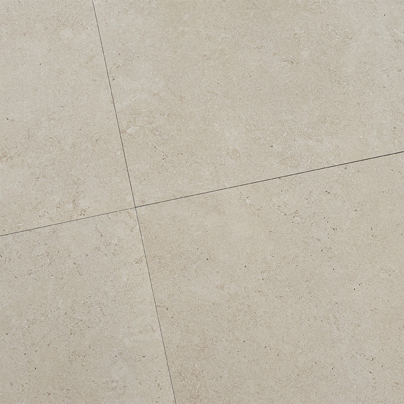 Azulejo de cerámica beige con textura de piedra; juntas finas que forman una cruz; superficie mate y veteada, parte de un suelo interior austero.