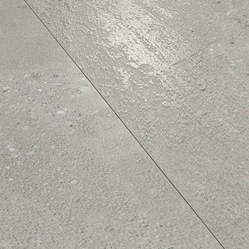 Carrelage gris clair composé de deux dalles séparées par un joint diagonal fin; surfaces légèrement granulées avec taches et reflets d'humidité.