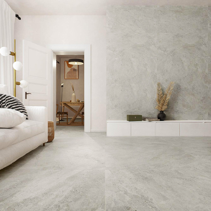 Azulejo cinza claro fosco cobrindo piso e parede; sala minimalista com sofá branco, luminária de piso, móvel baixo com vaso seco e porta aberta para outro cômodo.