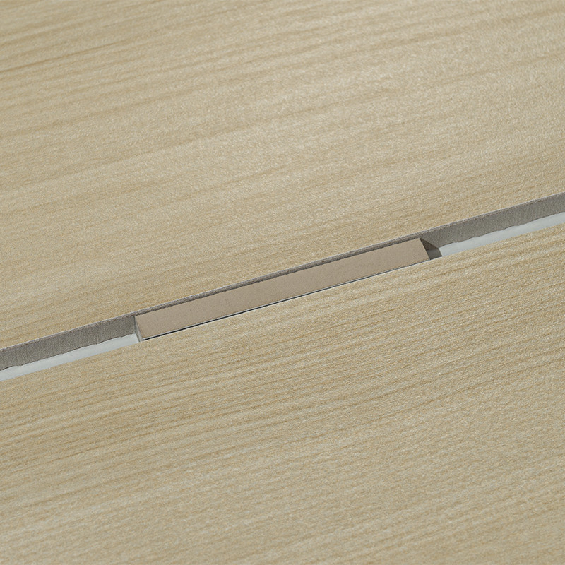 Rectangular tile fitted into a narrow joint on a light wood surface with horizontal grain; hollow and grey filler material visible in the cut.