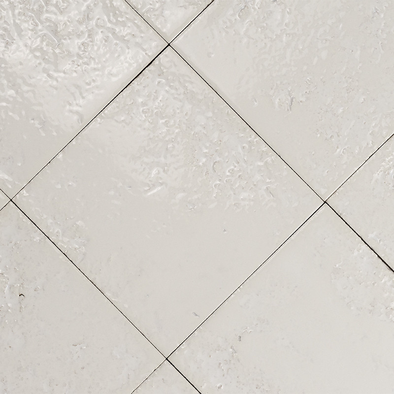 Azulejo blanco en patrón diagonal; juntas finas y pequeñas grietas; superficie ligeramente rugosa y brillante; varios azulejos contiguos formando un suelo o pared.