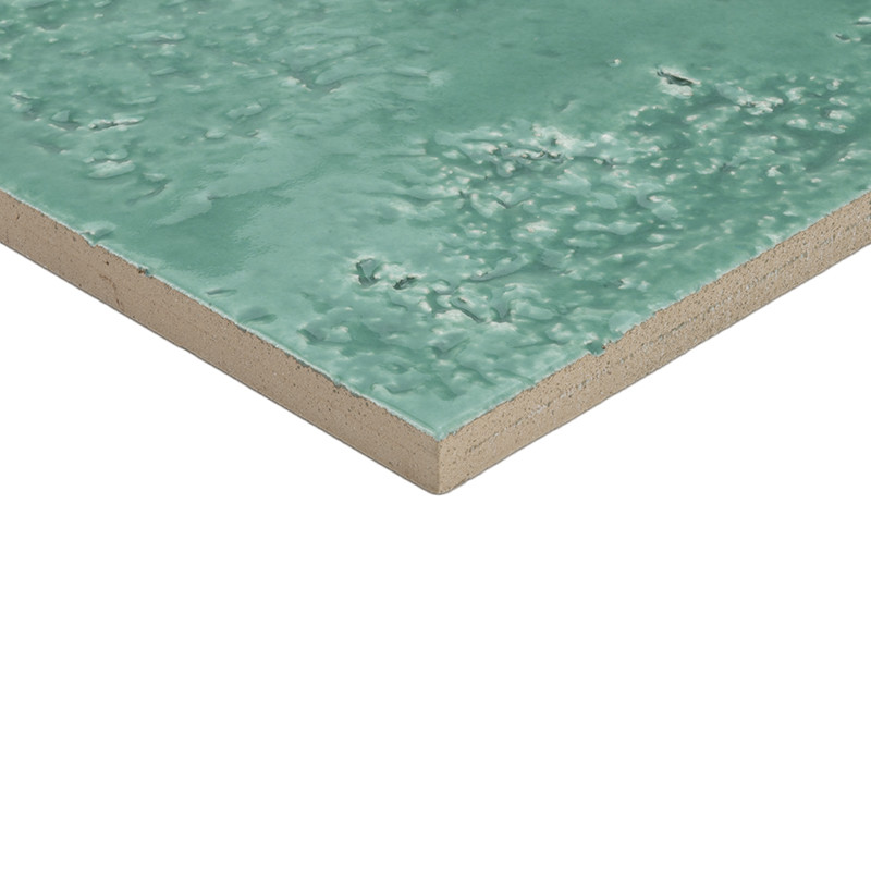 Tegel met geglazuurde turkooizen, licht onregelmatige structuur en kleine putjes; zichtbare beige zijkant, diagonaal geplaatst tegen een witte achtergrond.