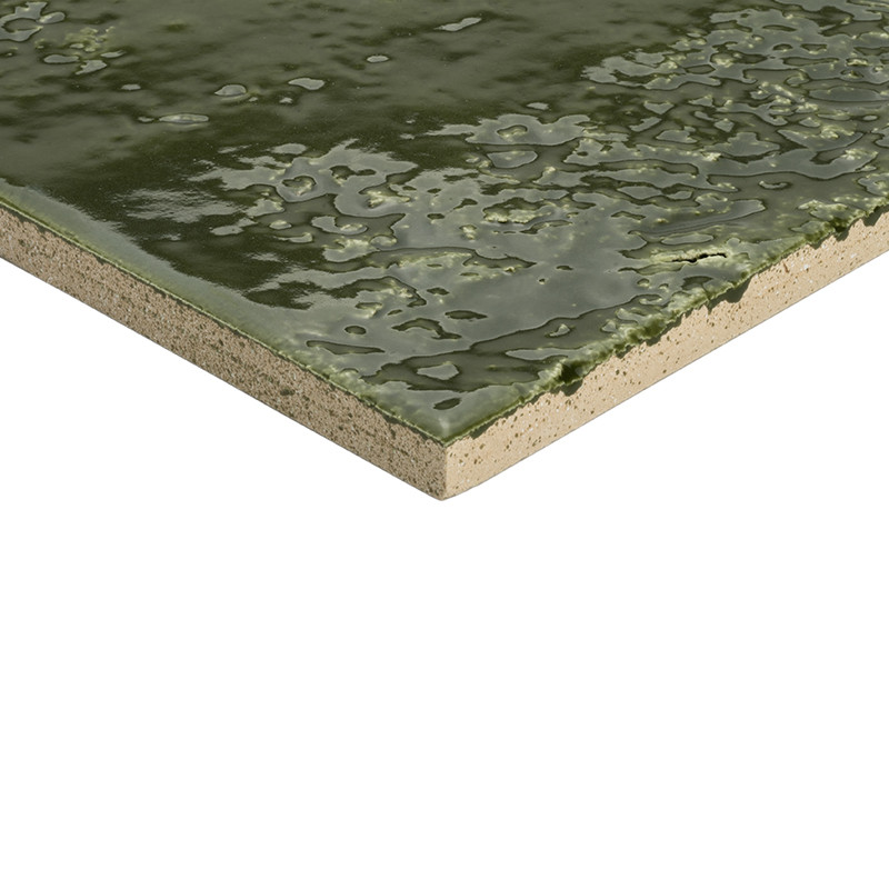 Ceramic tile: tile corner with glossy dark green glaze and irregular texture; edge reveals beige ceramic body; close-up shot on white background.