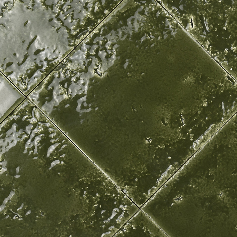 Dark green ceramic tile, glazed and with an irregular texture; arranged in a diagonal pattern with clear joints and bright reflections indicating a wet or polished surface.