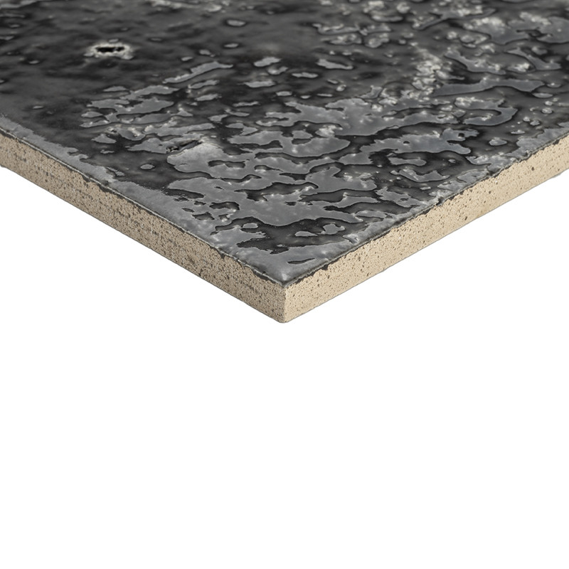 Carreau de carrelage noir brillant texturé, motifs irréguliers rappelant gouttes, angle en gros plan montrant épaisseur et support beige, présenté sur fond blanc.