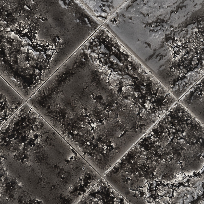 Azulejo cuadrado con superficie rugosa y moteada gris oscura; dispuesto en patrón romboidal, con juntas visibles y brillo irregular que sugiere humedad.