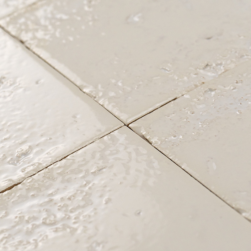 Azulejo cerâmico esmaltado bege, superfície brilhante e irregular com gotas; encontro de quatro peças e rejuntes visíveis, possivelmente revestimento de parede ou piso.