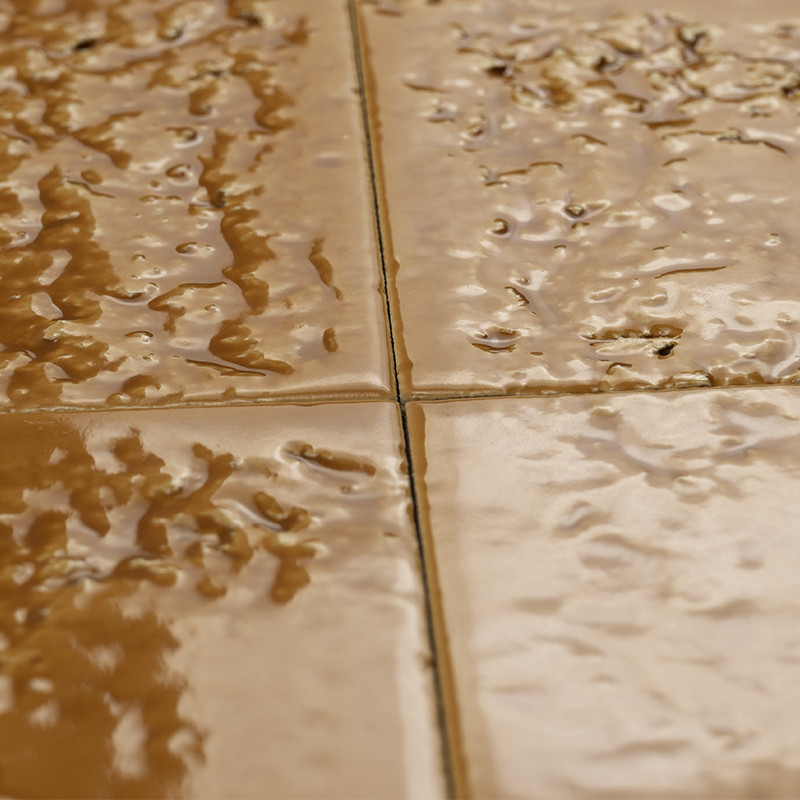 Carrelage brun lustré, joints fins formant une croix; surface mouillée avec reflets et petites irrégularités, plan rapproché centré sur la jonction de deux carreaux.