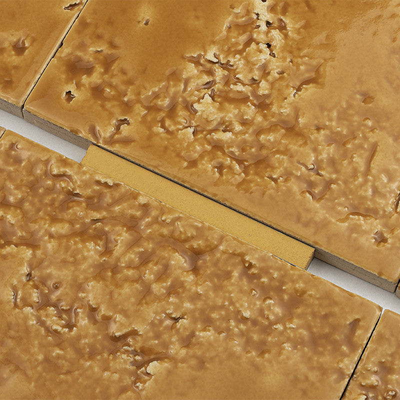 Textured brown tile with an irregular surface; visible joint between tiles with yellow plastic spacer and gray grout around it, close-up of its joint.