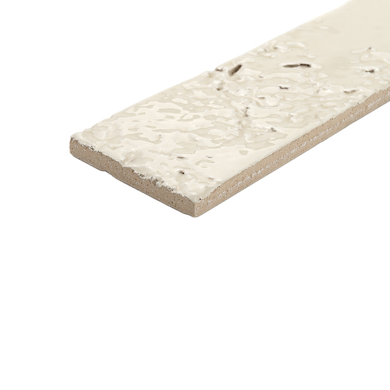 Azulejo rectangular alargado con borde visto y superficie esmaltada crema texturizada con pequeñas vetas oscuras; dispuesto en ángulo sobre fondo blanco.