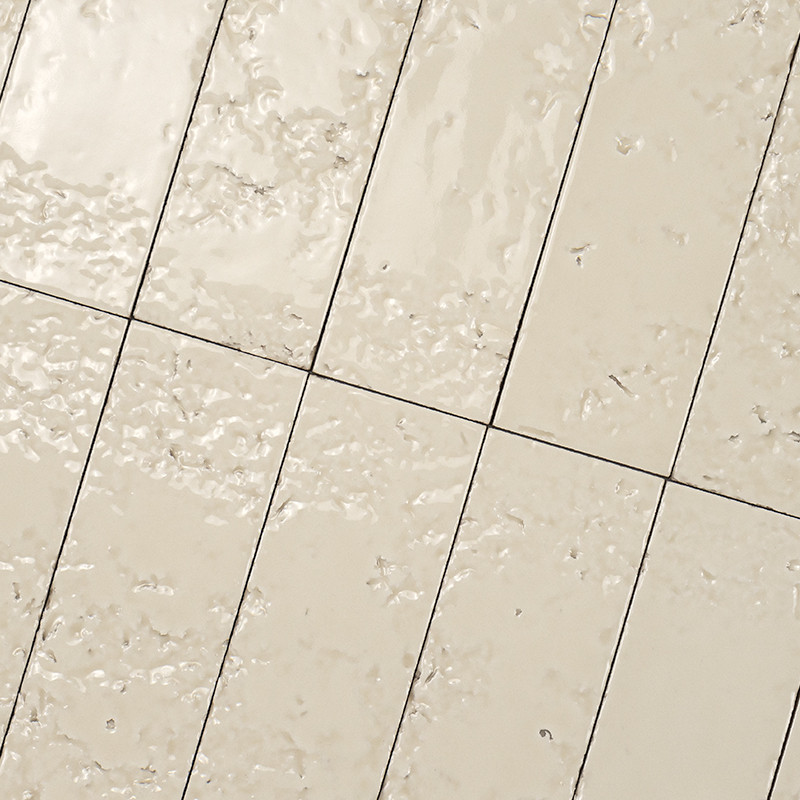 Azulejos creme retangulares brilhantes com textura irregular e sujeira leve; rejunte escuro formando linhas diagonais, aparenta piso ou parede molhada com respingos.