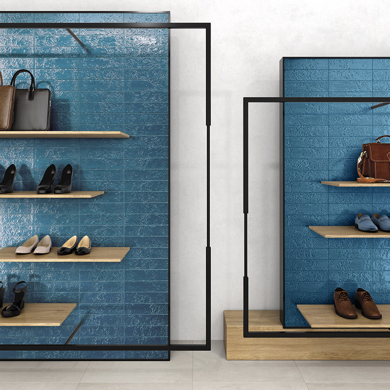 Carrelage mural bleu texturé en panneaux, encadré par structures métalliques noires; étagères en bois présentant chaussures et sacs dans un présentoir boutique sur sol clair.
