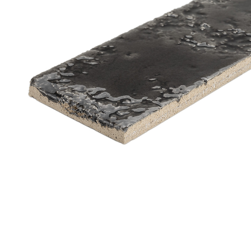 Azulejo rectangular esmaltado negro brillante, bordes irregulares y superficie con textura vidriada; canto y base cerámicos beige sin esmaltar; mostrado en ángulo sobre fondo blanco.