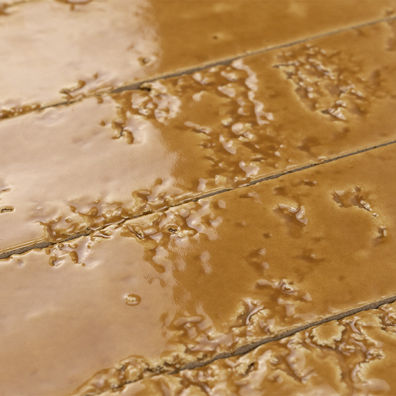 Carrelage en lames céramiques brunes à glaçure brillante et relief irrégulier, joints fins gris formant lignes parallèles; surface satinée reflétant légèrement la lumière.