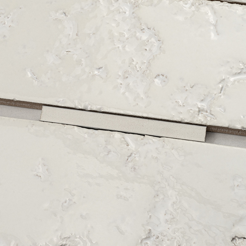 Carrelage : deux carreaux blancs marbrés séparés par un joint gris étroit où repose une cale plastique rectangulaire beige.