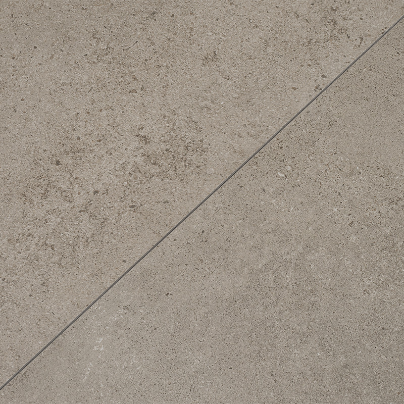 Wahrscheinlich Fliese mit diagonal verlaufender Fuge; raue hellgraue Betonoptik, feine dunkle Sprenkel und Körnung, matte Oberfläche.