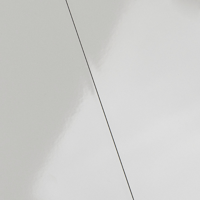 Carrelage blanc cassé à surface brillante, fissure fine et noire diagonale traversant la dalle; léger reflet et dégradé gris autour.