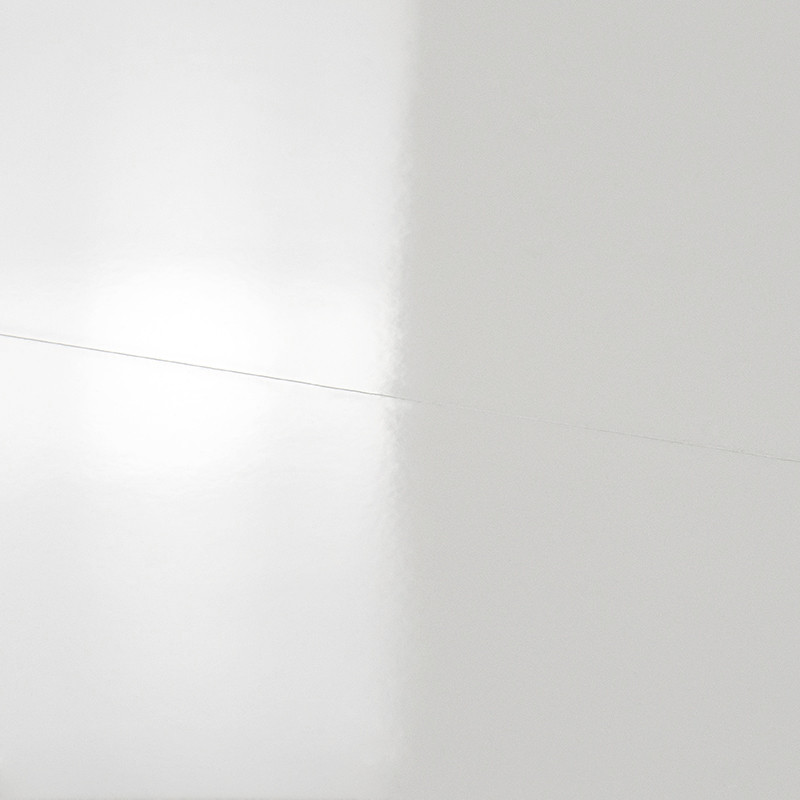 Azulejo blanco brillante con una fina grieta diagonal; refleja luz y muestra una junta vertical que delimita un azulejo contiguo.