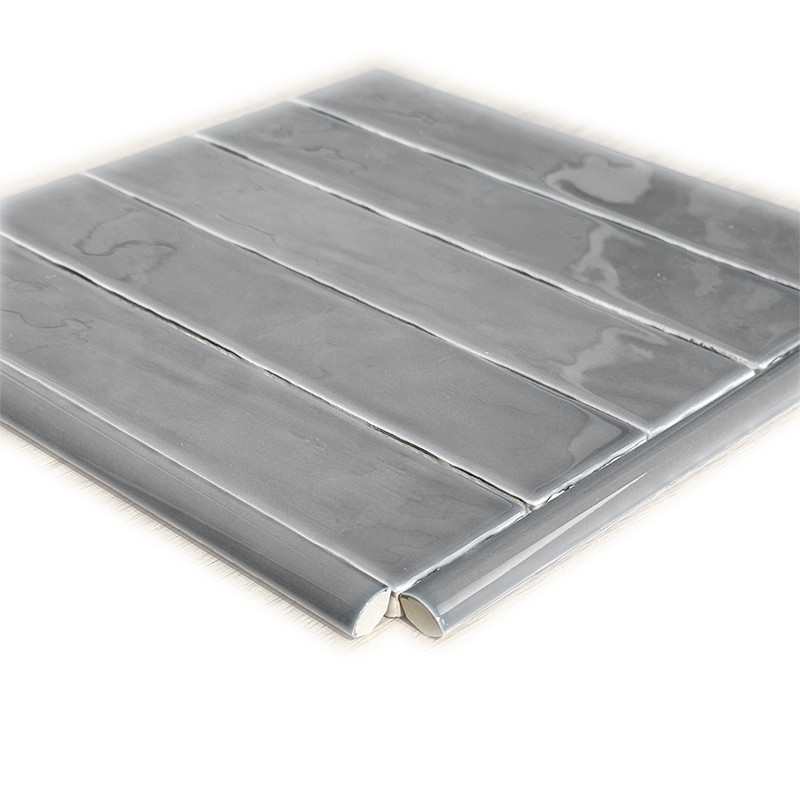 Carrelage gris brillant rectangulaire en rangées horizontales, joints pâles visibles; plan rapproché d’un échantillon posé sur fond blanc, reflets luisants sur les surfaces.