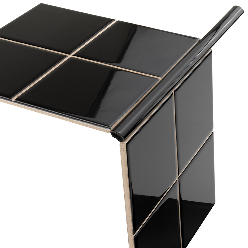 Glossy black tiles forming an L-shaped corner: four pieces visible on the surface and edge, clear joints and a rounded metallic finish; white background.