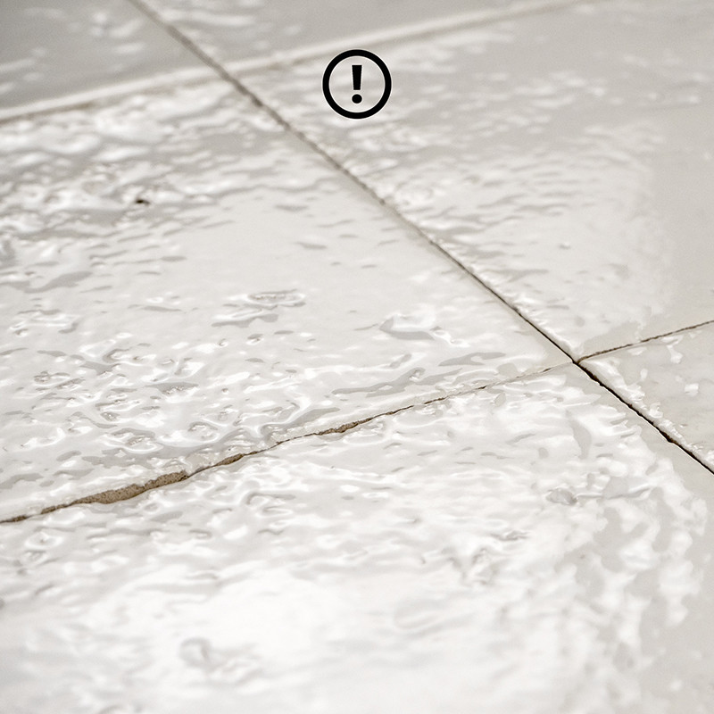 Carrelage blanc brillant, carreaux légèrement irréguliers et craquelés; joints foncés visibles; surface ondulée et réfléchissante suggérant finition émaillée.