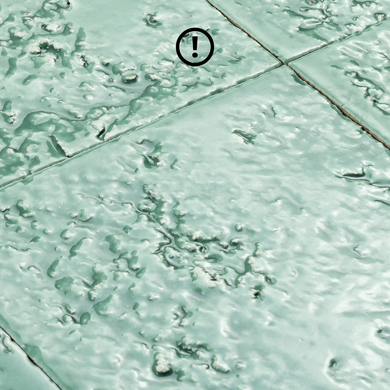 Azulejo verde-pálido com acabamento vítreo e textura enrugada; juntas delineiam quadrados, sugerindo piso cerâmico antigo ou superfície revestida.