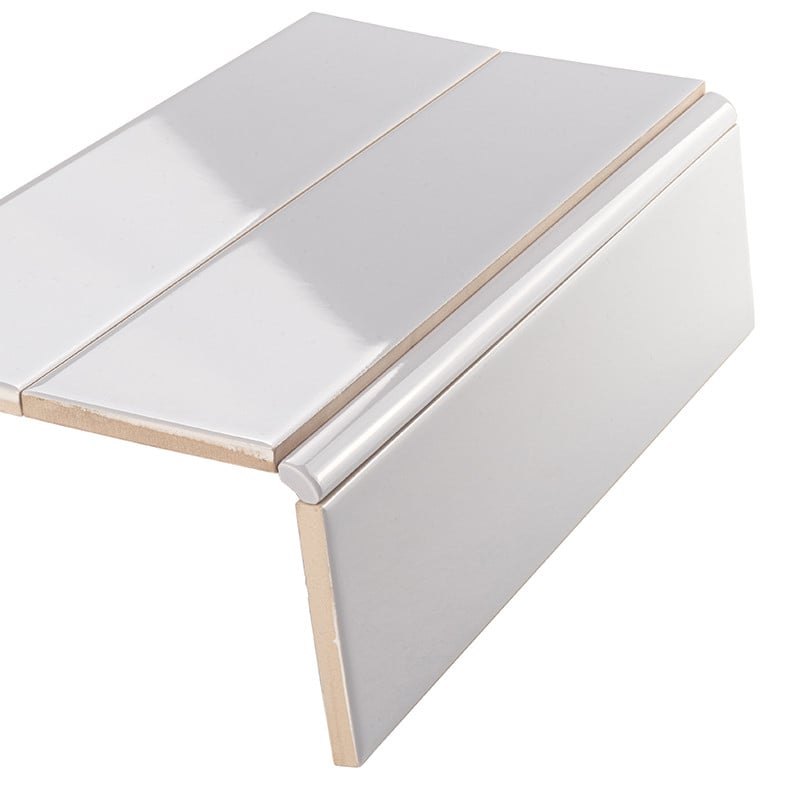 Weiße glänzende Keramik-Fliese mit braunem Trägermaterial, ausgestattet mit abgerundeter Abschlussleiste (Bullnose), auf weißem Hintergrund schräg angeordnet, Kanten und Profil sichtbar.